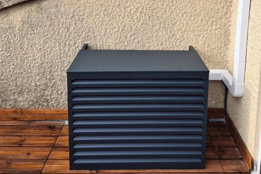 Unité extérieure de climatisation masquée par un coffre aluminium à lames ajourées, sur une terrasse en bois