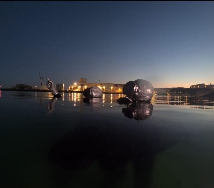 Les sculptures des nageurs émergeant de l'eau, à la tombée de la nuit